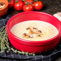 Bowl of mushroom cream soup with fried champignon mushrooms and vegetables on black stone background. Rustic style. Close up.