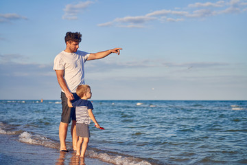 Young Caucasian dad with little son walk warm summer day along the sea coast. Summer family...