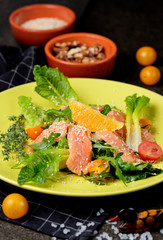 Cold salmon salad with green leaves, cucumber, avocado, lime and tomato on black stone background. Top view with copy space. Rustic style.