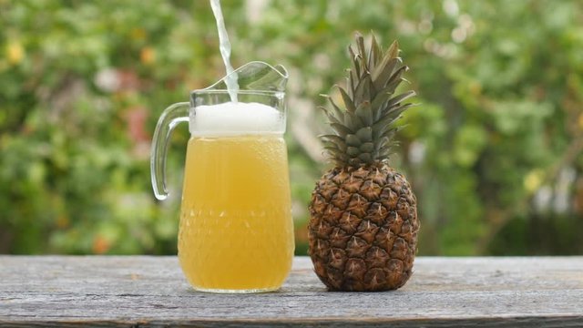 Yellow juice is poured into a jug on a wooden table. Orange or pineapple juice. Delicious healthy food.