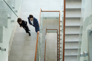 Overview of two young business people in formalwear walking upstairs