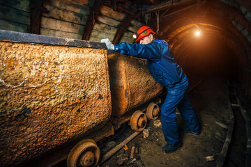 A miner in a coal mine stands near a trolley. Copy space.