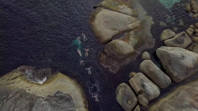 Plano de drone con grupo de personas nadando en el mar cerca de una playa de agua cristalina 4K