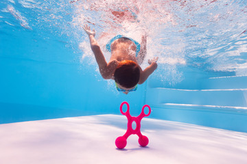 Little boy dive deep to reach the toy swimming underwater in the pool wearing googles