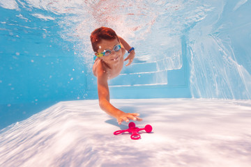 Little happy child dive deep to reach the toy swimming underwater in the pool wearing googles