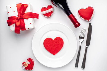 Table setting for Valentine's Day - white plate, wine, gift, kitchen appliances, hearts on a white background