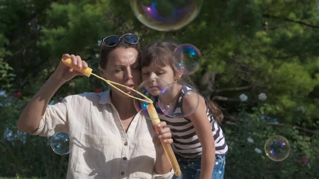 Mother blow soap bubbles. The family is having fun with soap bubbles. Little girl with her mother blow soap bubbles in a summer park.