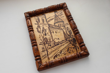 A wooden picture depicting the fortress wall and town of the city, made using the technique of pyrography. The picture is decorated with carved wooden frame and varnished.