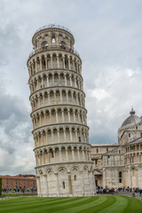 The Leaning Tower of Pisa is a bell tower surrounded by visitors and tourists near the cathedral in the Italian city of Pisa