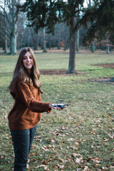 Young woman with a drone perched on her hand and a green park in background.