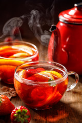 Fruit hot tea with the addition of oranges, lemons, strawberries mandarins and raspberries in a glass cups on a  wooden table. Healthy hot drink