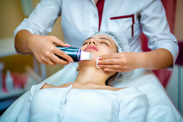 Woman receiving ultrasonic facial exfoliation at cosmetology salon. Procedure clearing clogged...