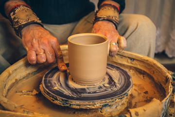The master forms a clay cup on a potter's wheel. A potter's hands preparing a clay pot. Close-up.