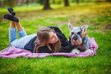 Pretty girl with his Schnauzer dog at nature park outdoor is standing and posing in front of camera. Portrait of owner and Rough collie dog enjoys, resting and petting together on city street.