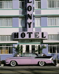 This is the Colony Hotel on the strip of South Beach Miami. There is a purple and black vintage car parked in front of the hotel. - obrazy, fototapety, plakaty