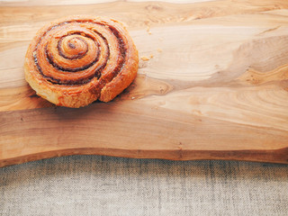 One traditional freshly cooked cinnamon swirl, pastry product on a wooden board surface and simple table cloth. Close up.