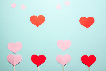 Fototapeta na wymiar Paper hearts of different sizes fly up from red and pink hearts on wooden sticks on blue background. Valentines day concept. Flat lay top view