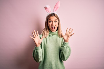 Young beautiful woman wearing easter rabbit ears standing over isolated pink background celebrating crazy and amazed for success with arms raised and open eyes screaming excited. Winner concept