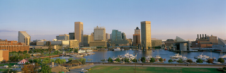 This is the skyline in daylight showing the inner harbor and city lights. There are boats moored in the harbor - obrazy, fototapety, plakaty