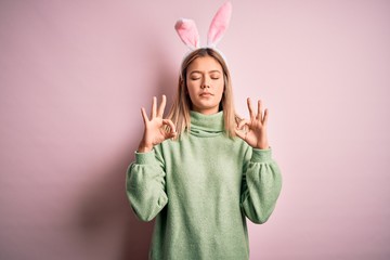 Young beautiful woman wearing easter rabbit ears standing over isolated pink background relax and smiling with eyes closed doing meditation gesture with fingers. Yoga concept.