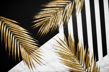 Exotic golden branch palm leaf on black and marble backdrop. Copy space. Decorative trendy template for flat lay, advertising