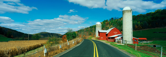 This is a country road with a farm on the right hand side of the road. It has a red barn and silo. © spiritofamerica