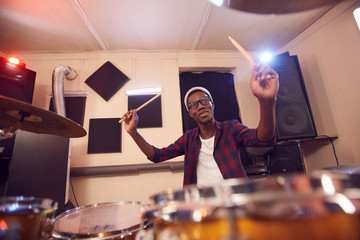 Fototapeta na wymiar Portrait of young African-American man playing drums with contemporary music band during rehearsal or concert in studio, copy space