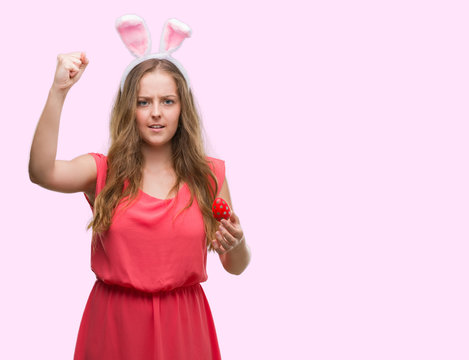 Young blonde woman wearing easter bunny ears annoyed and frustrated shouting with anger, crazy and yelling with raised hand, anger concept