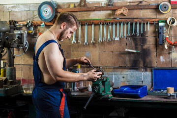 Professional car mechanic working near table with different instruments and keeping in his hand spark plug from auto engine.