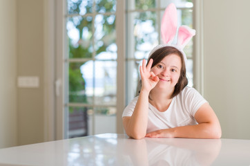 Down syndrome woman at home wearing easter rabbit ears doing ok sign with fingers, excellent symbol