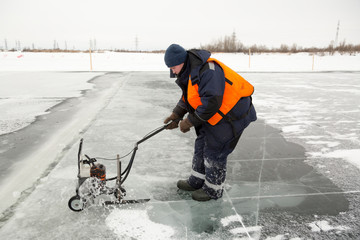 Worker cuts out ice blocks in size on the ice of a frozen lake