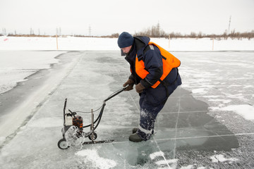 Worker cuts out ice blocks in size on the ice of a frozen lake
