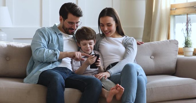 Smiling parents with kid son relax on sofa using smartphone