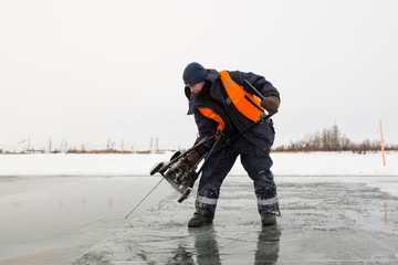 Fototapeta na wymiar Worker cuts out ice blocks in size on the ice of a frozen lake
