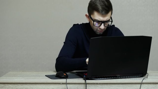 Male hacker in glasses and do hacker attack on laptop, man freelancer programmer