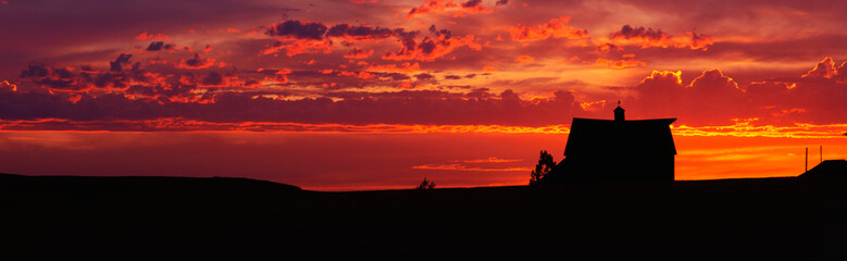 Fototapeta na wymiar This is a farm at sunset. The farm house is silhouetted against an orange sky.