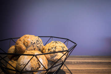 Brotkorb mit selbst gebackenen und geformten Brötchen auf einem Holzbrett vor einem lilanen Hintergrund 
