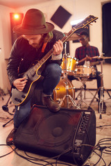Full length portrait of contemporary young man playing electric guitar solo leaning on amplifier...