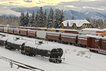 rail yard in winter with trains, depot, and mountains in background, whitefish, montana