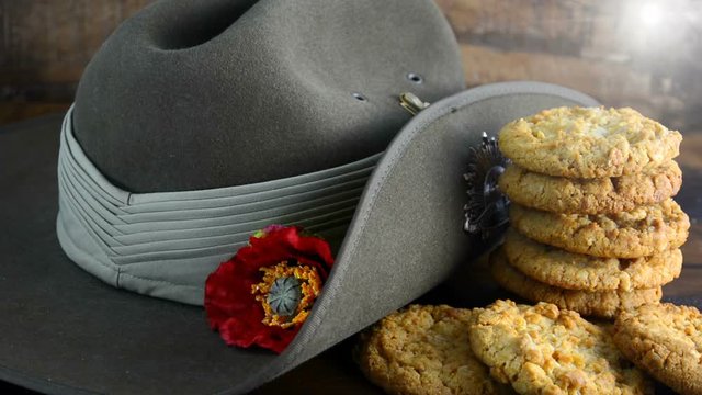 Australian Anzac biscuits with soldier slouch hat on dark vintage background with remembrance red poppy for Anzac Day or Remembrance Armistice Day. Placing last cookie on stack with lens flare.