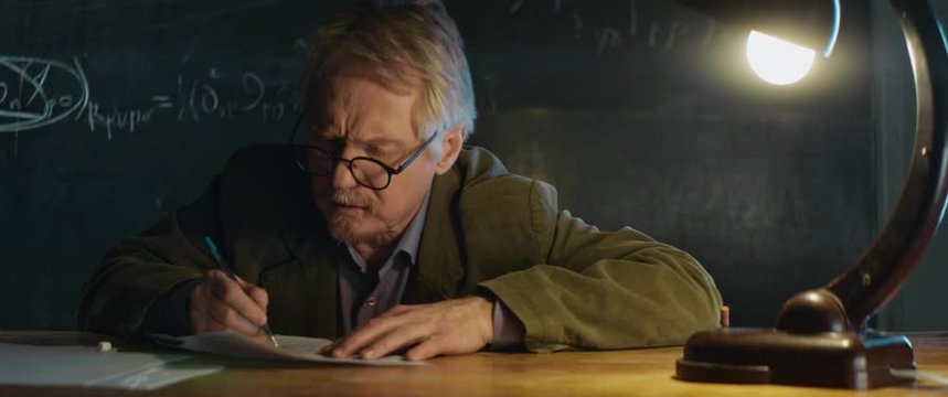 Elderly Professor in glasses working, writing smth on notebook. desk lamp light. late night, thinking cogitative process, origin of idea, research of invention, smart wise man