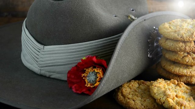 Australian Anzac biscuits with soldier slouch hat on dark vintage background with remembrance red poppy for Anzac Day or Remembrance Armistice Day. Slow panning with lens flare.