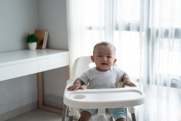 happy asian baby boy sitting on high chair smiling