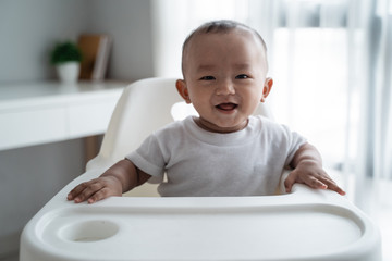 cute asian baby boy smiling to camera while eating sitting on high chair