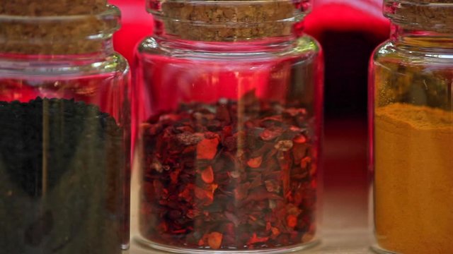 Selection of Jars with dried spices laid out in a row on wooden table. close up pan right 