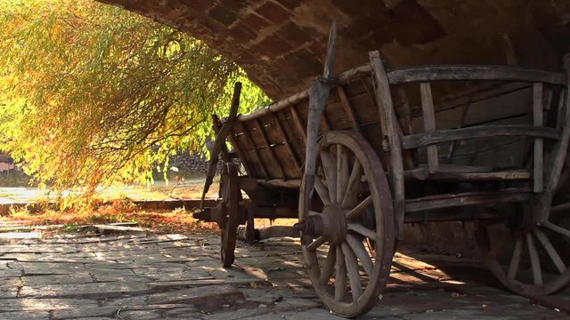 Wooden cart resting under archway with autumn sunlight coming through trees in the background 