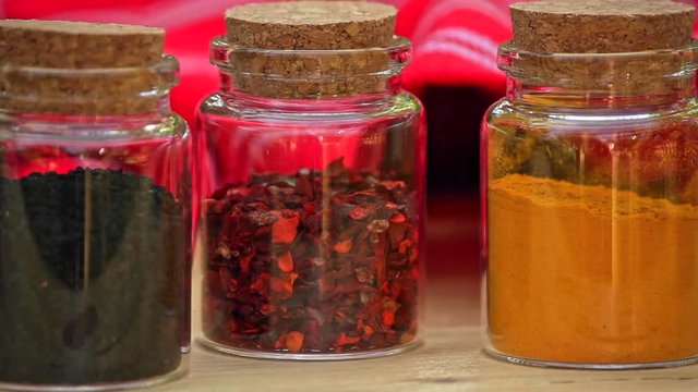 pan right cllose up view of selection of Jars with dried spices laid out in a row on wooden table