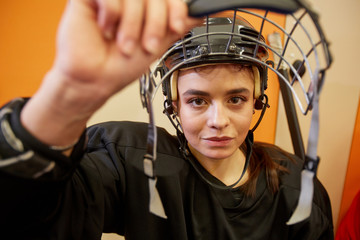 Closeup of female hockey player opening face guard and smiling at camera in locker room, copy space