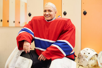 Fototapeta premium Portrait of young female hockey player smiling at camera while posing in locker room before match, copy space