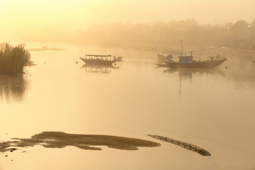 Traditional Vietnamese boats at misty morning river.